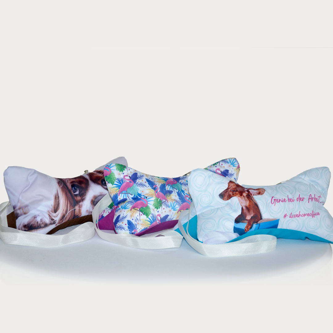 Drei bedruckte Nackenkissen, die jeweils unterschiedliche Tiermotive und Muster zeigen.