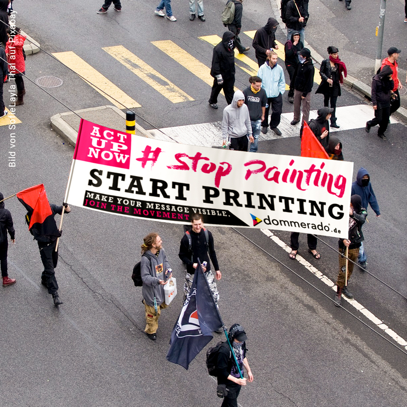 Ein großes, bedrucktes Banner wird während einer Demonstration über einer Straße gehalten.